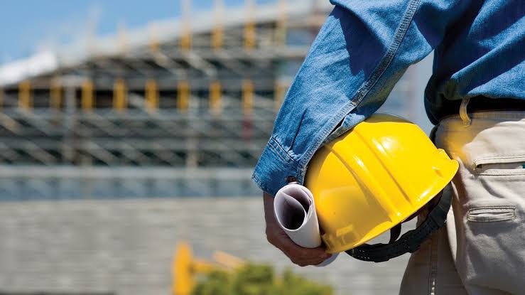 Site engineer holding a hard hat and rolled drawings in front of a structure under construction